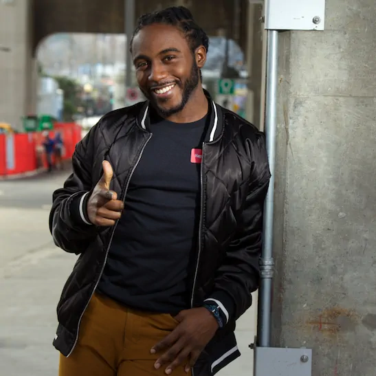 Chris Latham, host of Wait, That's a Business?, smiling and pointing at the camera on a city street.